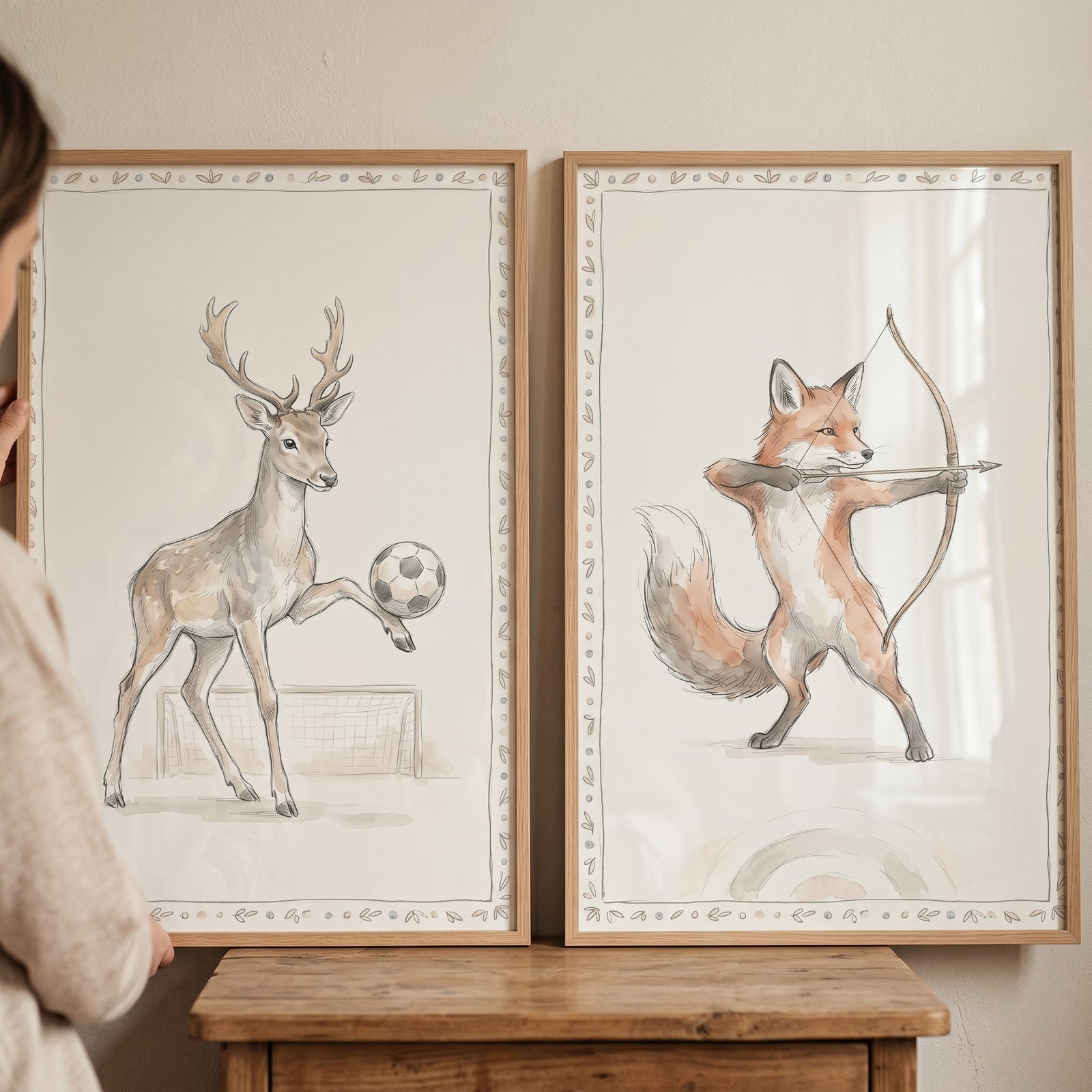 Soft watercolor athletic animals wall art set of 2: a deer plays soccer and a fox practices archery in wood frames.