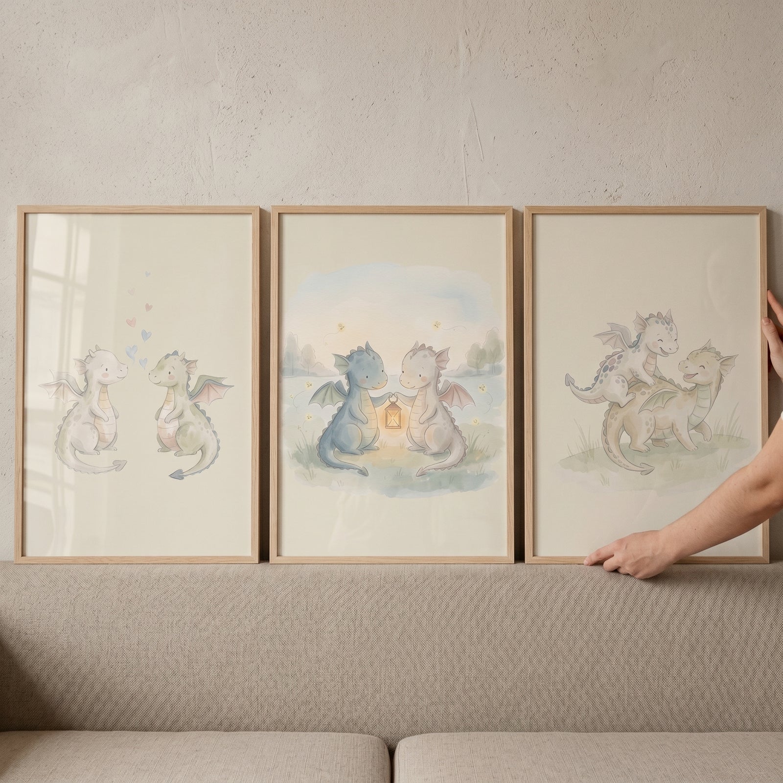 Soft watercolor baby dragons wall art set of 3 in light wood frames hanging above a neutral-toned sofa.