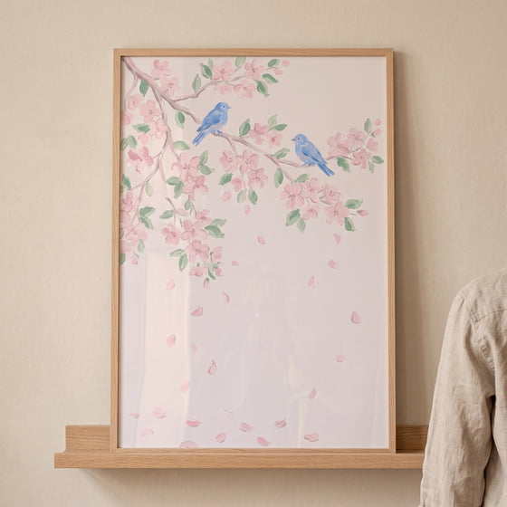 Soft watercolor blue bird wall art featuring two birds on cherry blossom branches, framed in light wood on a shelf.