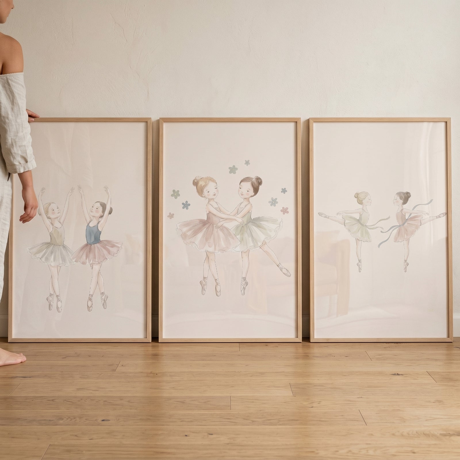 Framed soft watercolor little ballerina wall art set of 3 resting on a wood floor against a white wall.
