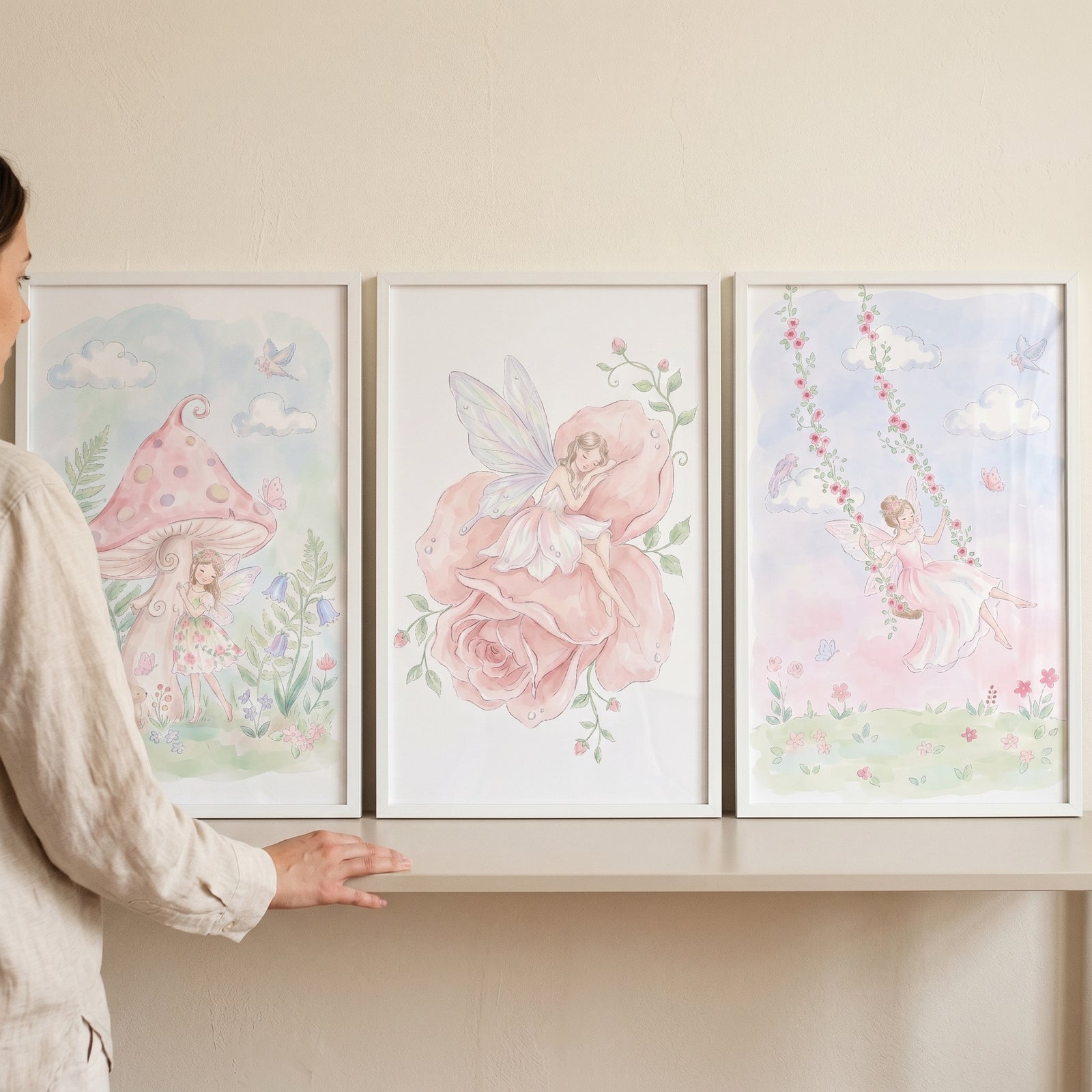 Soft watercolor pink fairy wall art set of 3 featuring fairies with a mushroom, a large rose, and a floral swing.