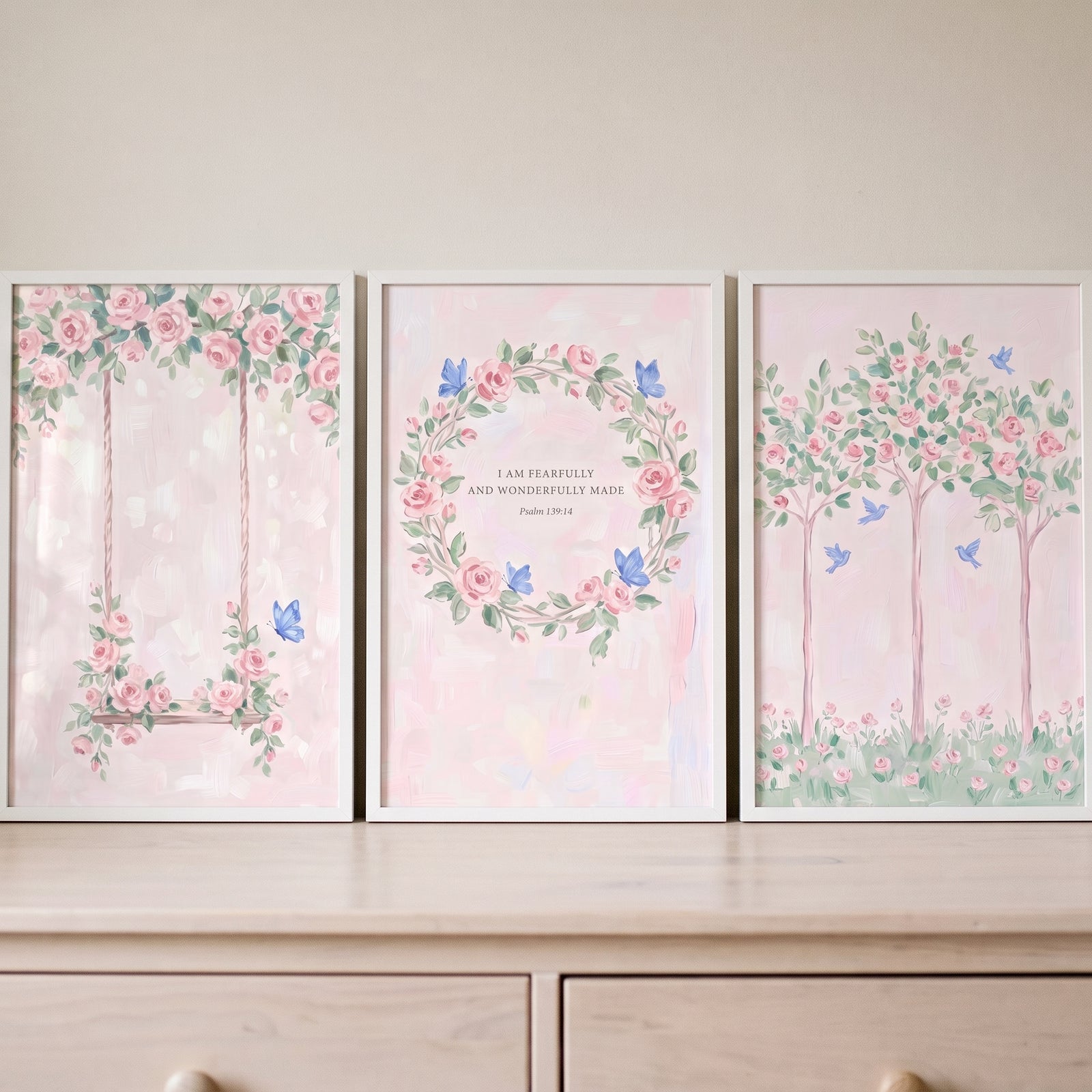 Soft watercolor pink rose floral wall art set of 3 with a swing, wreath with text, and trees on a light wood dresser.