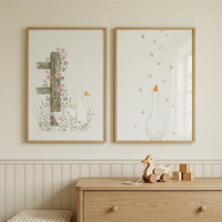 Two framed watercolor illustrations hang above a light wood dresser one showing a white duck beside a rustic wooden post with pink flowers and the other a duck looking up at falling pink petals. A wooden duck toy and alphabet blocks on the dresser add a playful cozy touch to the soft nature inspired nursery scene.