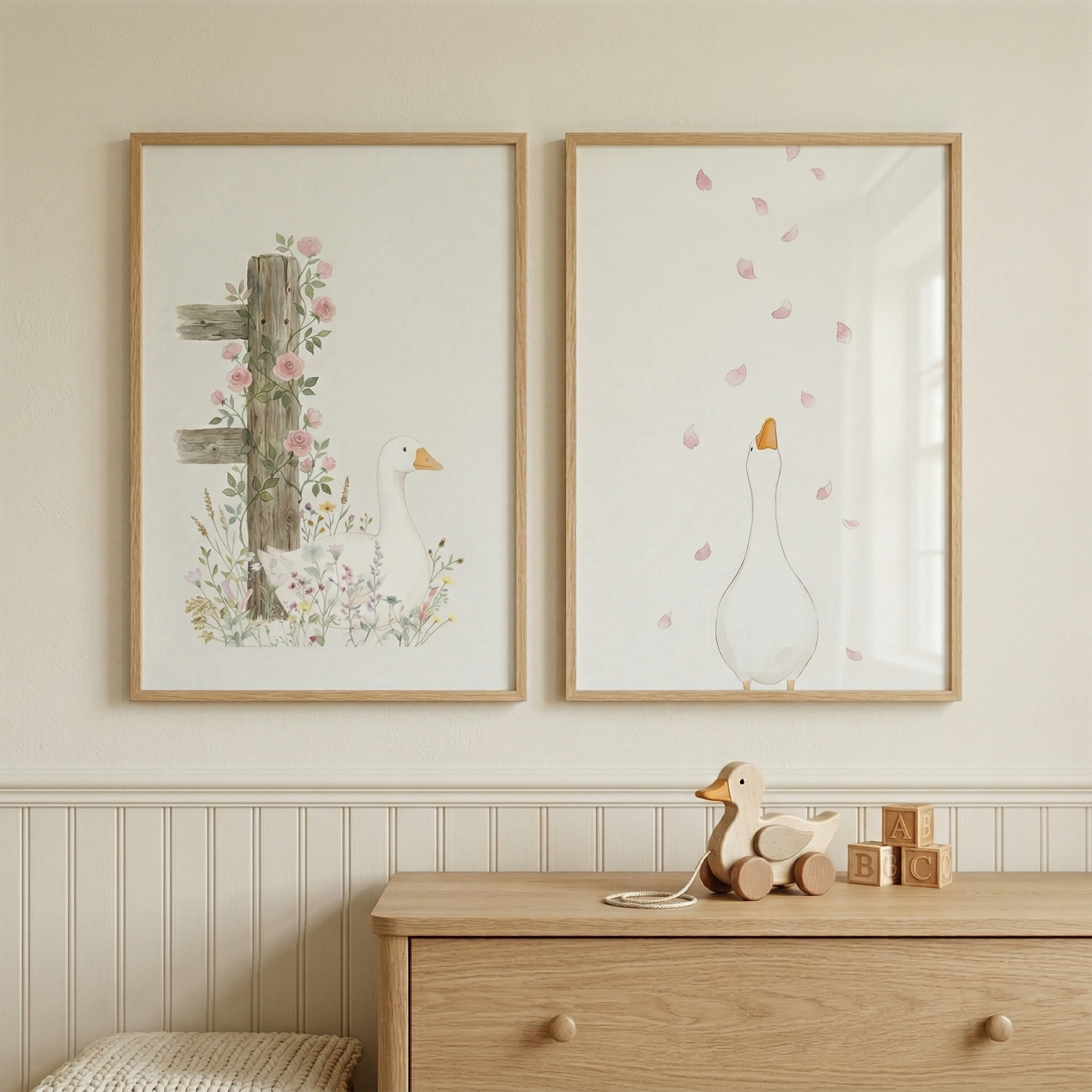 Two framed watercolor illustrations hang above a light wood dresser one showing a white duck beside a rustic wooden post with pink flowers and the other a duck looking up at falling pink petals. A wooden duck toy and alphabet blocks on the dresser add a playful cozy touch to the soft nature inspired nursery scene.