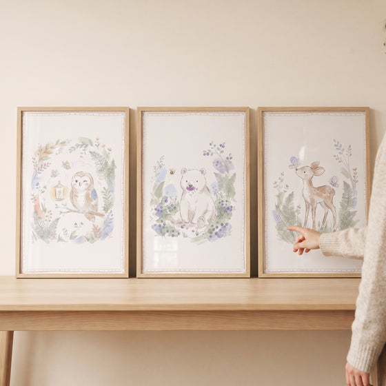Soft watercolor woodland animals wall art set of 3 featuring an owl, bear, and deer in light wooden frames on a table.