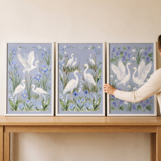 Sophisticated blue wildflower bird egret wall art set of 3 in white frames resting on a light wood table.