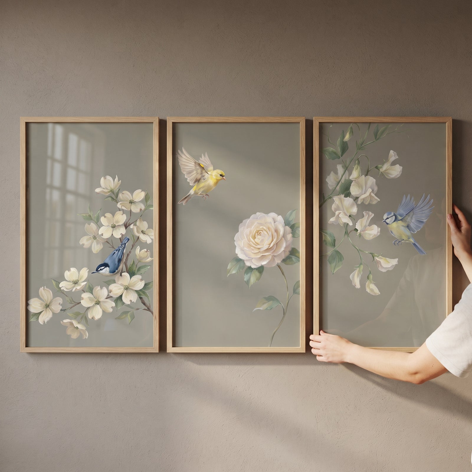 Hands hold a sophisticated sage botanical bird wall art set of 3 featuring white flowers and birds in light wood frames.