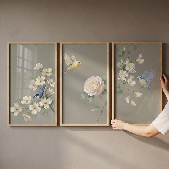Hands hold a sophisticated sage botanical bird wall art set of 3 featuring white flowers and birds in light wood frames.