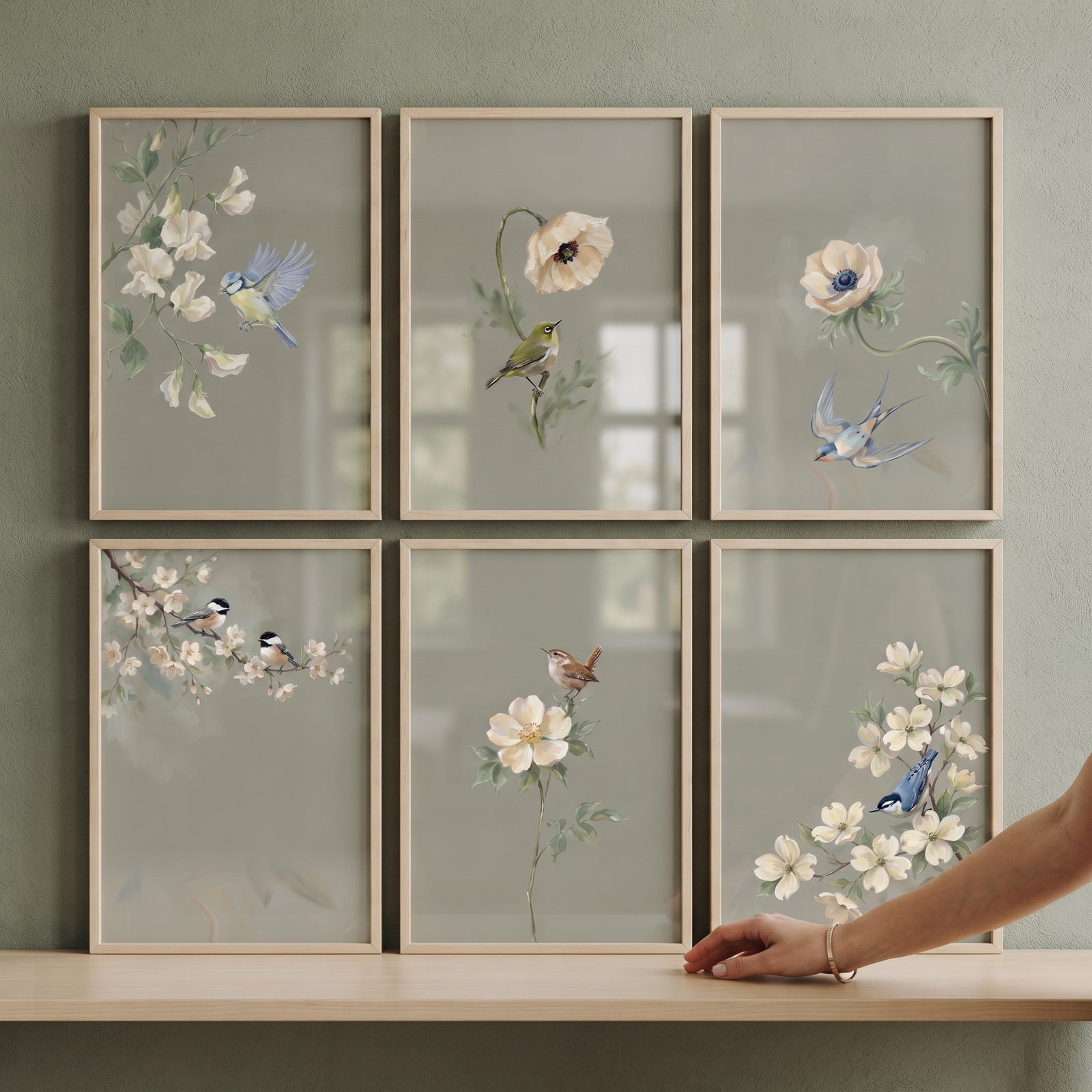 Sophisticated sage garden bird floral artwork set of 6 in light wood frames on a wall with a hand reaching toward a frame.