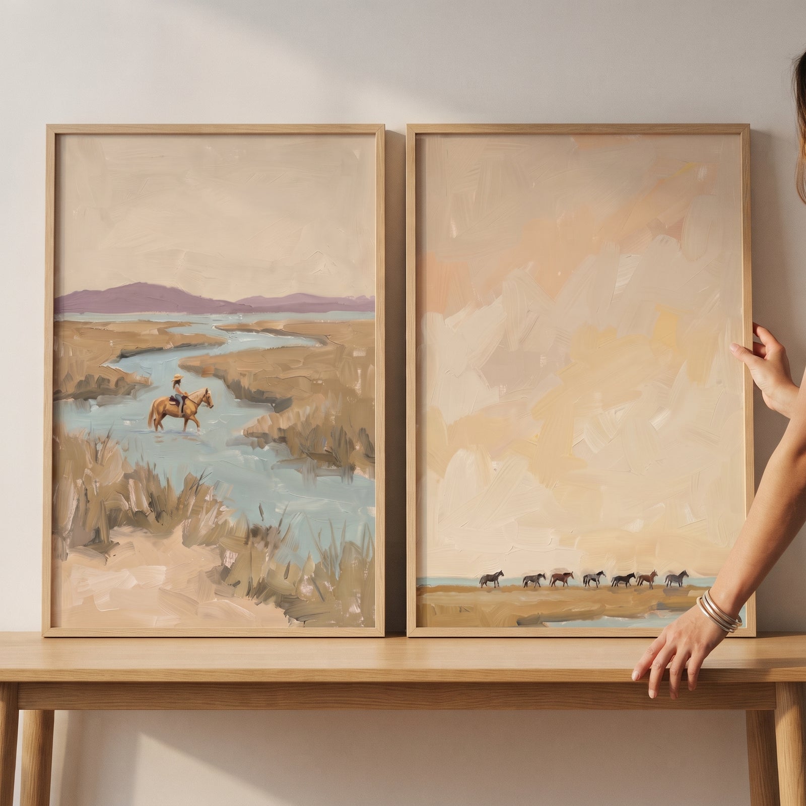 Hands adjust a sophisticated tan wetland horses wall art set of 2 featuring horses in a soft, muted marsh landscape.