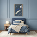 A serene bedroom with a celestial theme features light blue walls accented with classic panel moulding. In the center, a bed with a navy blue upholstered headboard is dressed in a comforter and pillows patterned with white stars. A chunky, cream-colored knit throw is layered over the foot of the bed. 

