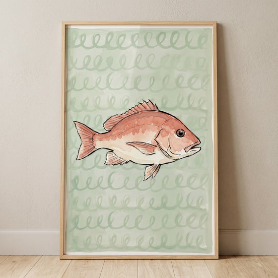 Spiral pattern sea bream fish wall art features a reddish fish on a green background in a wood frame leaning against a wall.