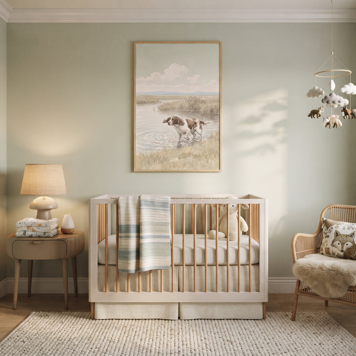 Nursery with a crib, lamp, and splashing water springer spaniel dog wall art on sage walls beside a wicker chair.