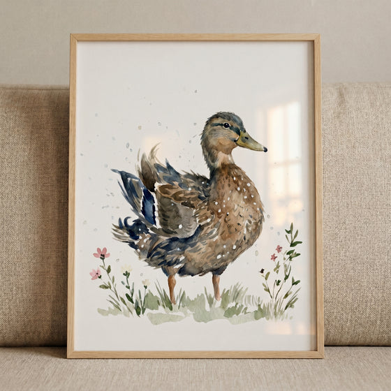 Splatter mallard duck wall art in a light wood frame shows the bird in a meadow with wild grass and small pink flowers.