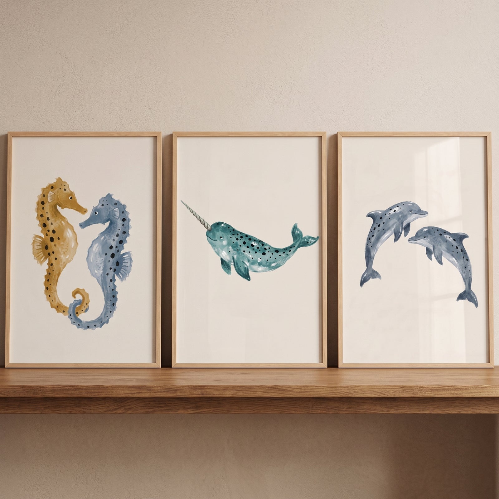 Seahorses, a narwhal, and dolphins in a spotted blue sea animal wall art set of 3 on a wooden shelf.