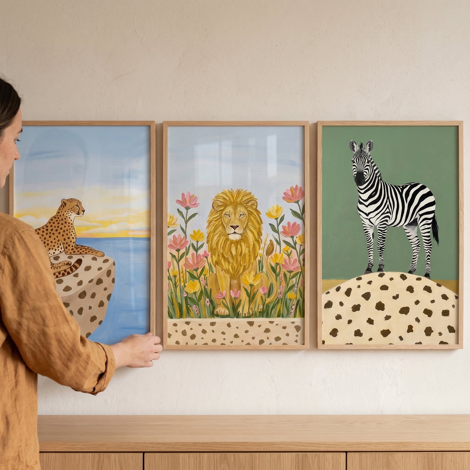 A person hangs a spotted ground safari animal wall art set of 3 featuring a cheetah, a lion, and a zebra.