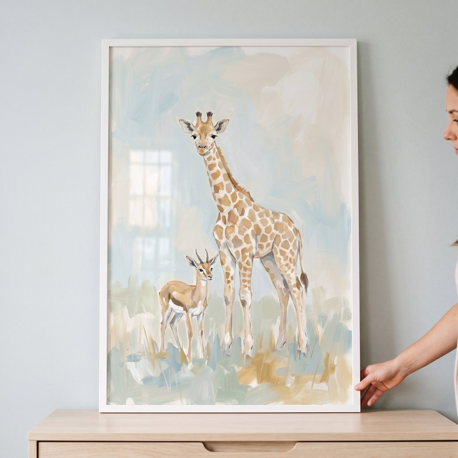 A person holds a framed spotted safari giraffe gazelle animals wall art piece with soft watercolor textures.