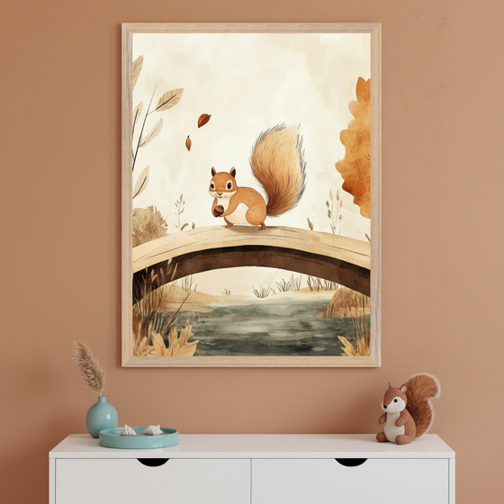 A framed illustration of a cute cartoon squirrel holding an acorn while standing on a wooden bridge over a small stream, surrounded by autumn leaves and earthy-toned trees. The artwork hangs above a white cabinet topped with a small plush squirrel, a turquoise vase with dried grass, and a matching tray, all against a warm terracotta wall.