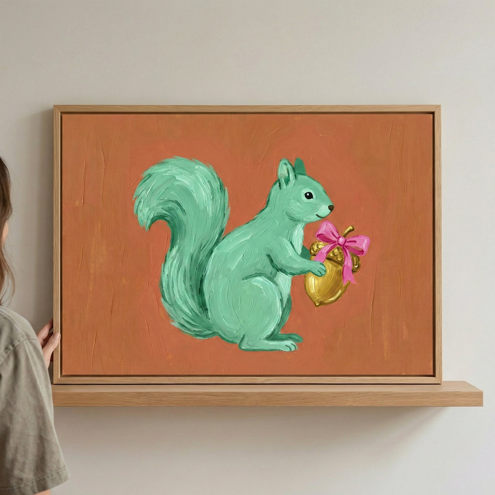 A cheerful painting of a mint green squirrel holding a shiny golden acorn tied with a pink ribbon, set against a warm, textured orange background. The whimsical style and soft colors give it a storybook charm.