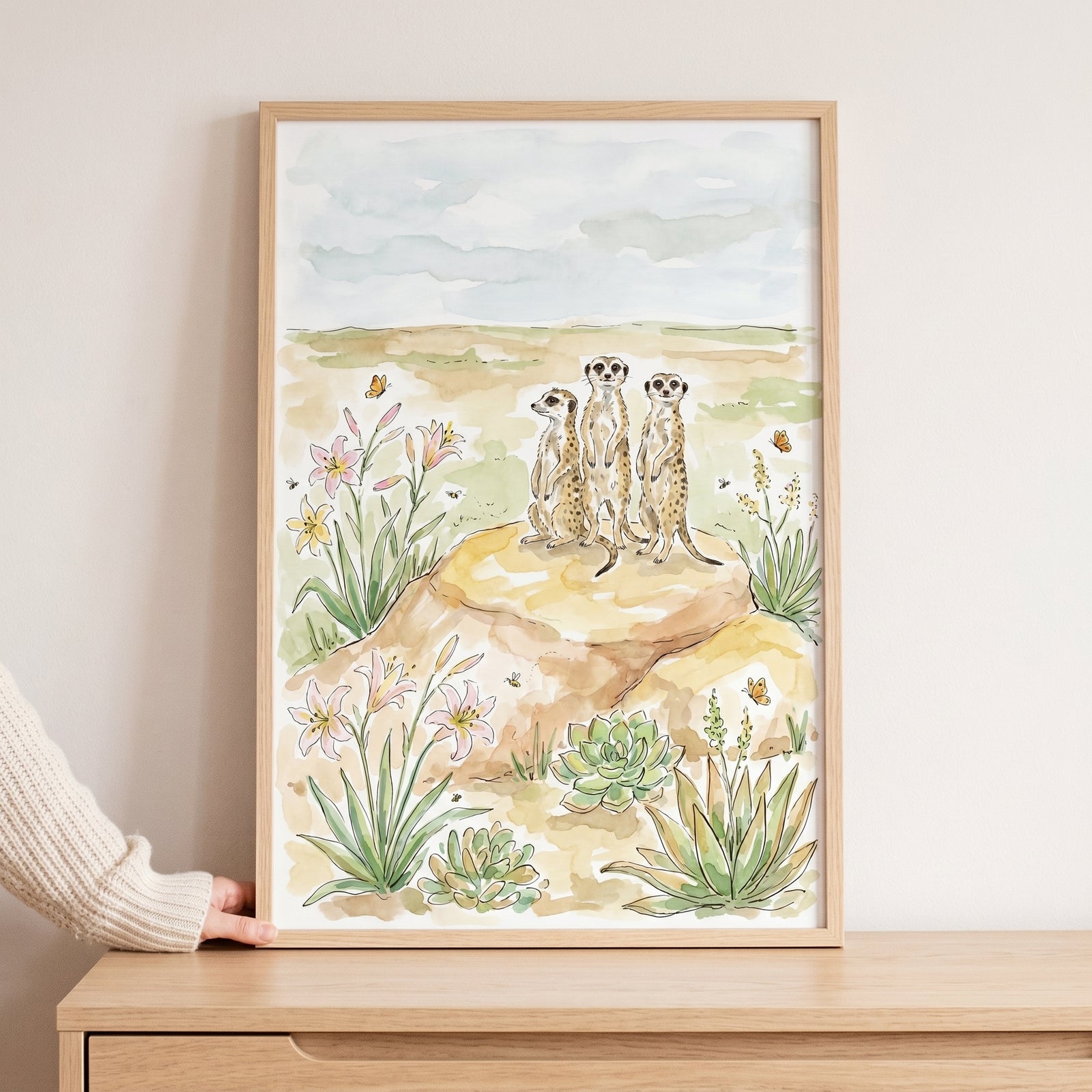 Watercolor standing lookout desert meerkats wall art features three animals on a rock among flowers and succulents.