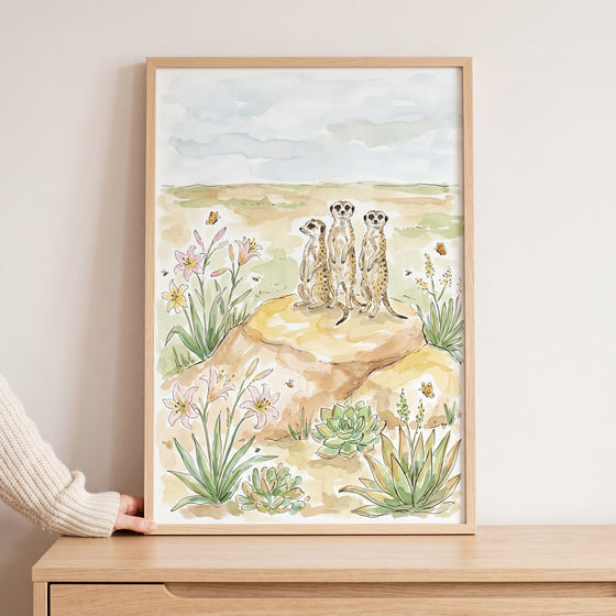 Watercolor standing lookout desert meerkats wall art features three animals on a rock among flowers and succulents.