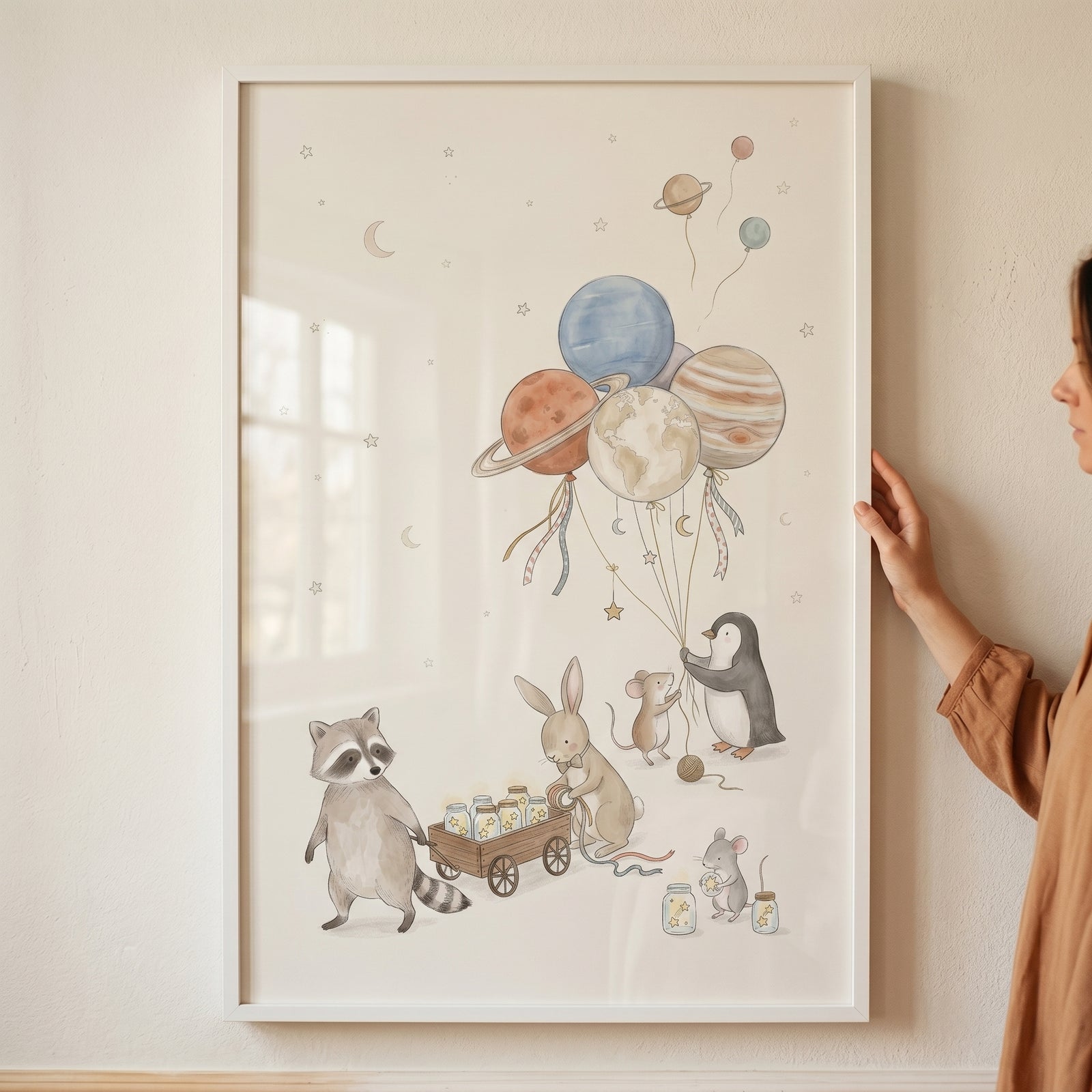 Hand holds framed star jar wagon animals wall art featuring a raccoon, bunny, and penguin holding planet balloons.