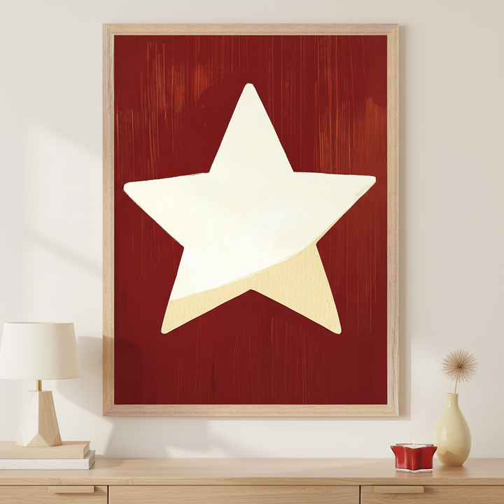 Modern room with a light wood dresser. A large framed print of a cream star on a brushed dark red background hangs centered above the dresser. Lamp and books on left, candle and vase on right.