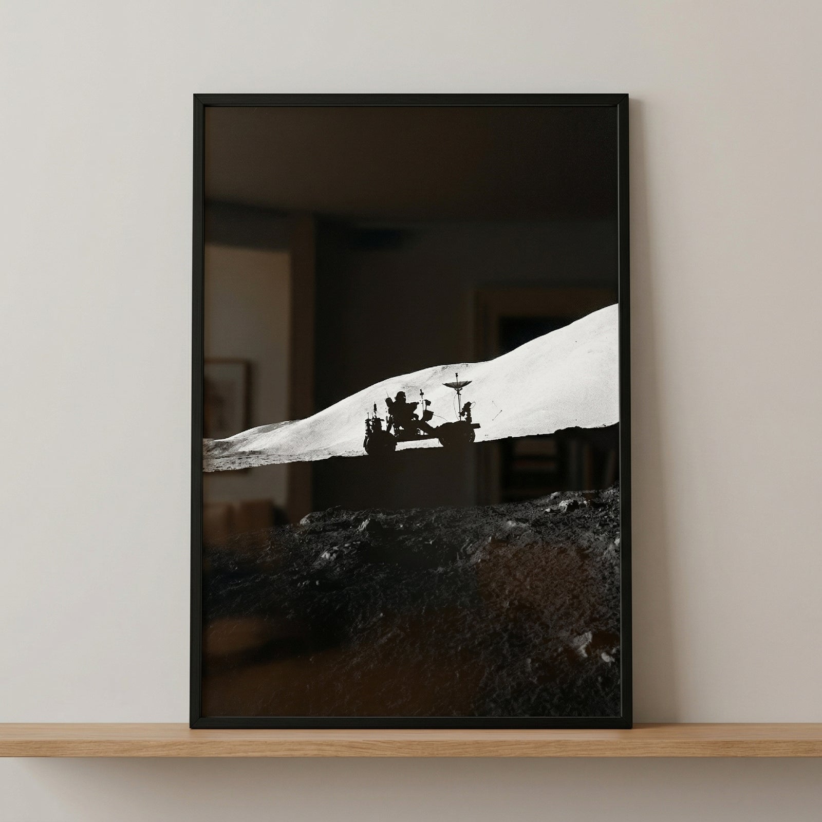 Stark silhouette lunar rover wall art on a wooden shelf depicts a vehicle on a white moon horizon against a black sky.