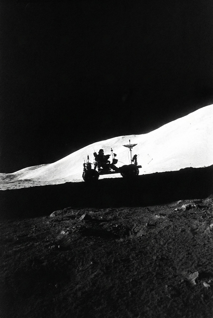 Silhouetted lunar rover sits along a ridge with a bright sunlit slope behind it and deep shadows in the foreground. The stark contrast highlights the vehicle’s outline against the vast, empty lunar landscape.
