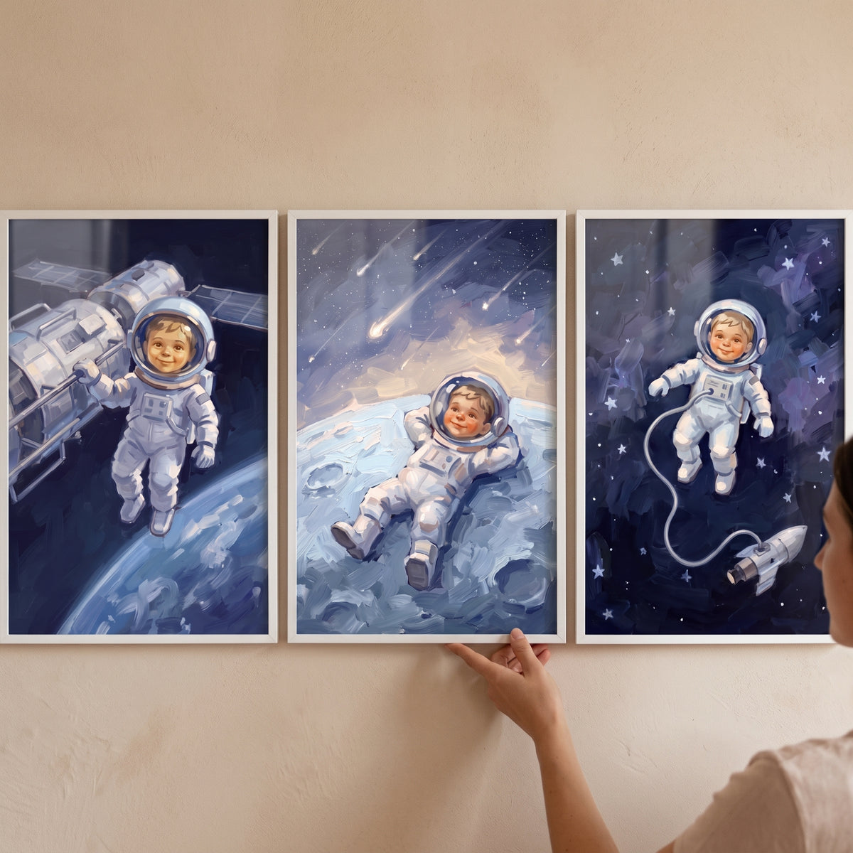 A person adjusts a starlit indigo baby astronaut wall art set of 3 featuring a small explorer in space.