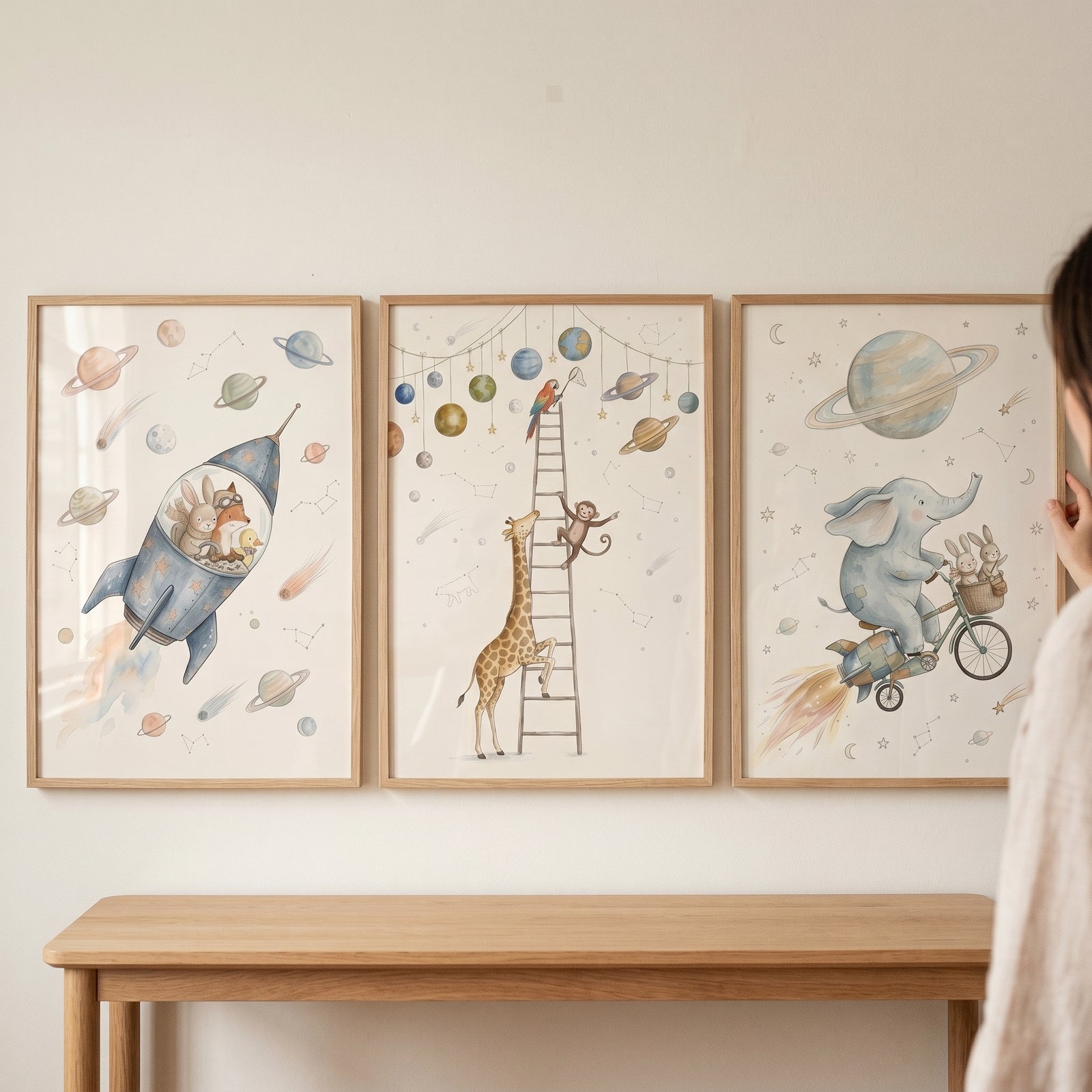 Starlit watercolor cosmic animals wall art set of 3 hangs above a wooden table with a rocket, giraffe, and elephant.