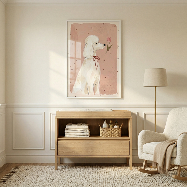 A framed illustration of a white poodle is the centerpiece of this calm, neutral-toned room, hung on a wall with elegant white wainscoting. The dog in the art is depicted in profile with a small red bow around its neck, facing a single pink tulip against a dusty rose background accented with tiny brown stars. Below the framed piece sits a light-colored wooden changing table featuring an open shelf with neatly stacked white towels and a small woven basket holding bottles. 