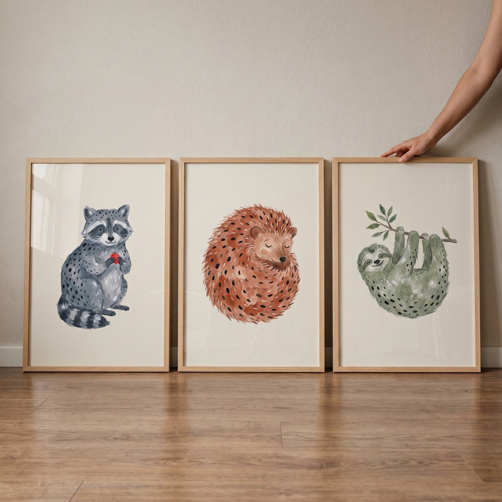 Stippled earthy neutral animals wall art set of 3 with a raccoon, hedgehog, and sloth in light wood frames on a floor.