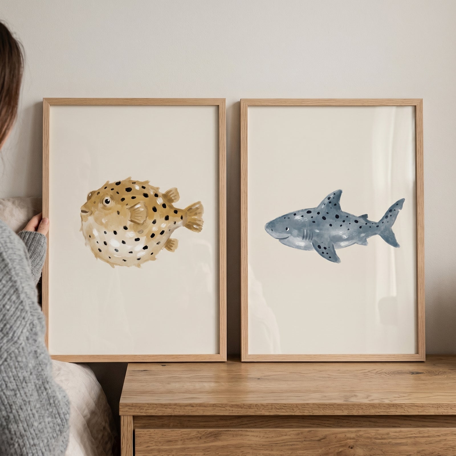 Stippled neutral ocean animals wall art set of 2 including a pufferfish and shark in light wood frames on a dresser.