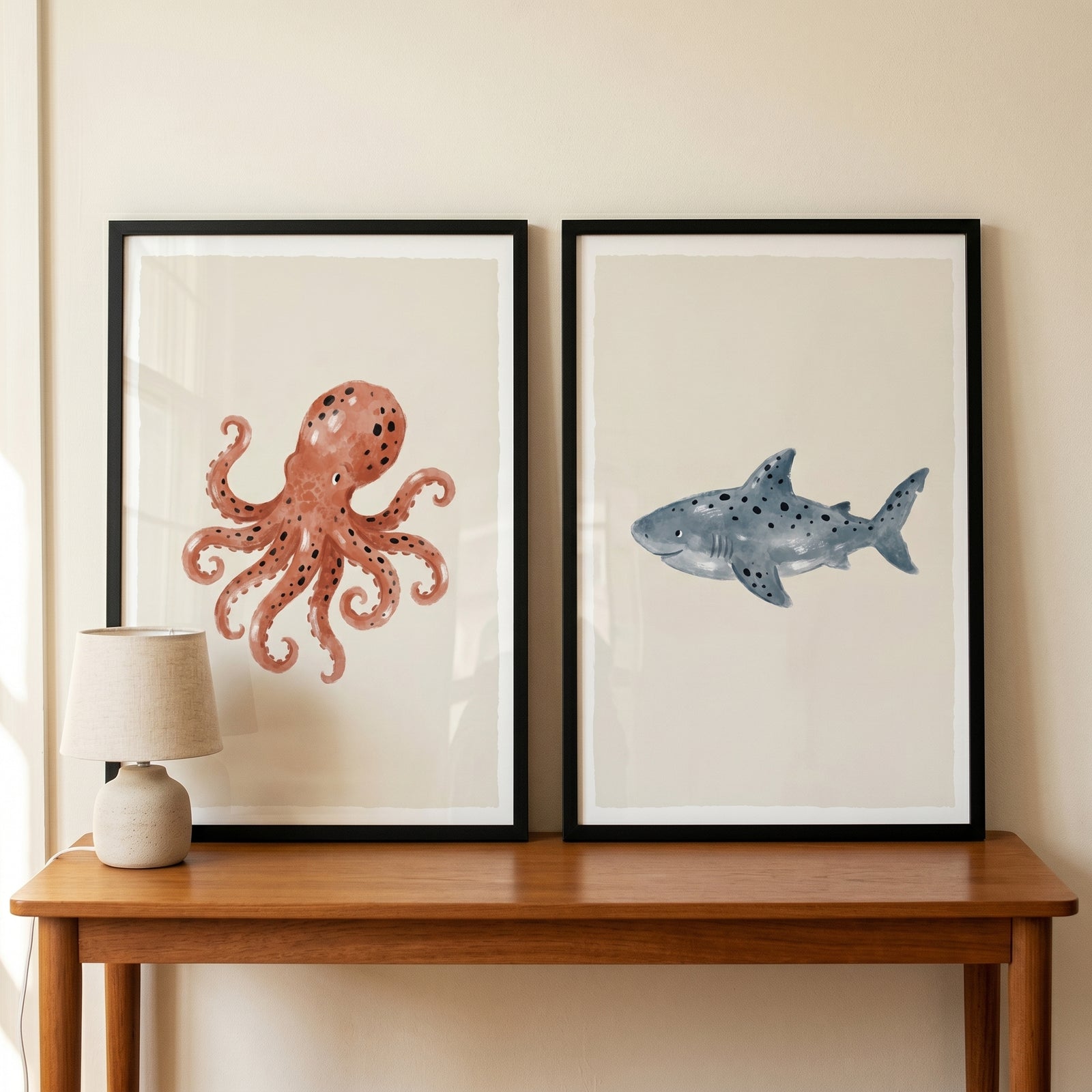 Stippled watercolor sea creature wall art set of 2 featuring an octopus and shark above a wooden table with a small lamp.