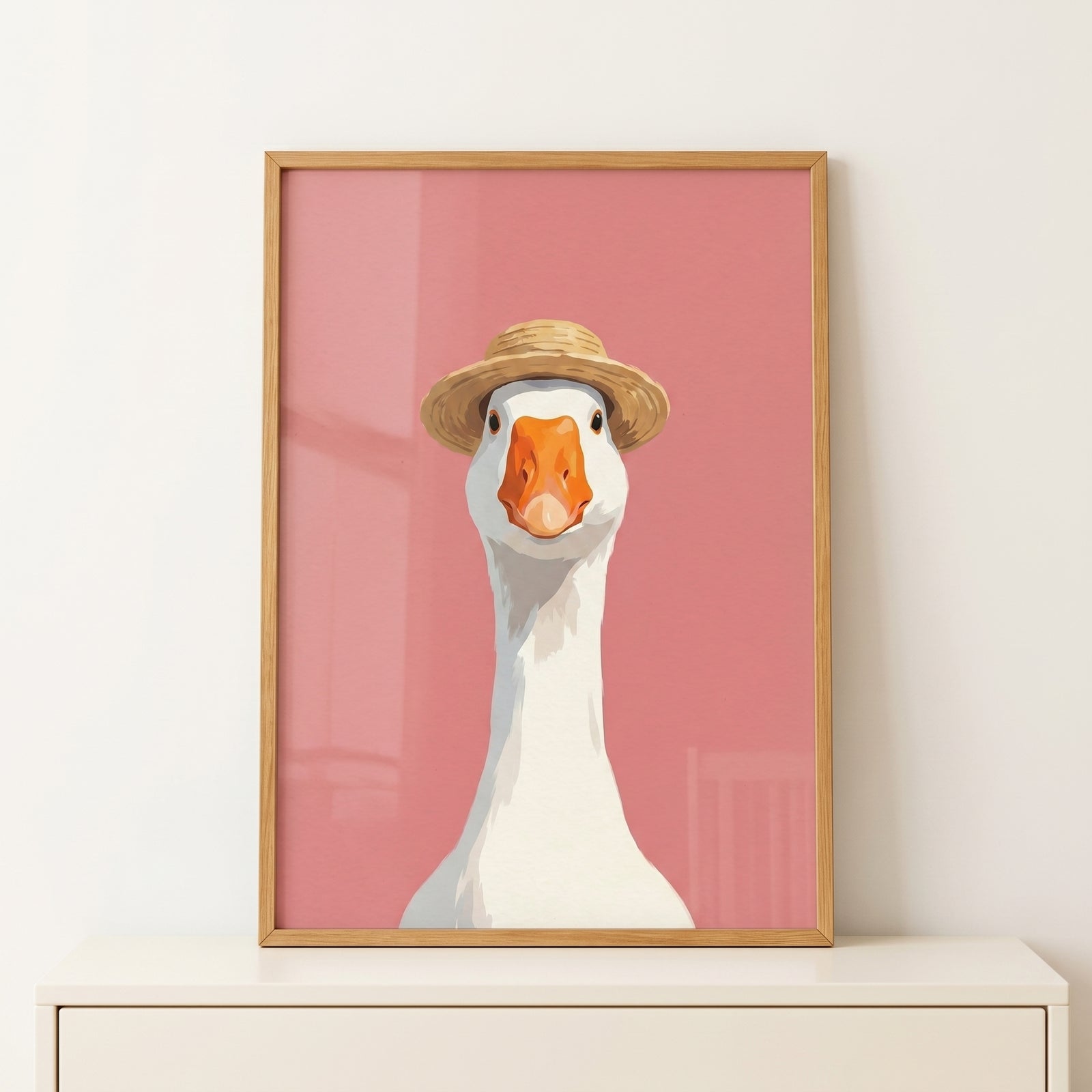 Framed straw hat white goose wall art with a pink background rests on a white dresser.
