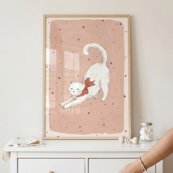 A framed illustration of a white cat stretching is displayed on a light-colored wall above a white wooden dresser. The cat is shown in a playful stretch, wearing a red and white checkered bow around its neck. The artwork features a soft pink rectangular background decorated with small, scattered brown and gold stars. The piece is encased in a simple, light-toned wood frame. 