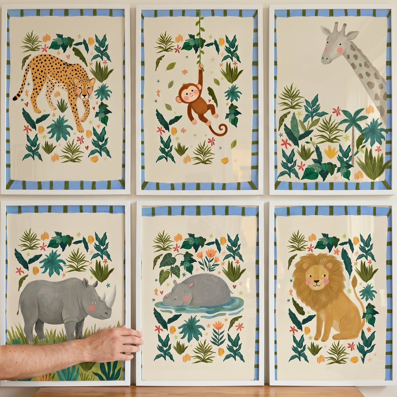 A hand adjusts a striped border jungle animal wall art set of 6 featuring a cheetah, monkey, giraffe, rhino, hippo, and lion.
