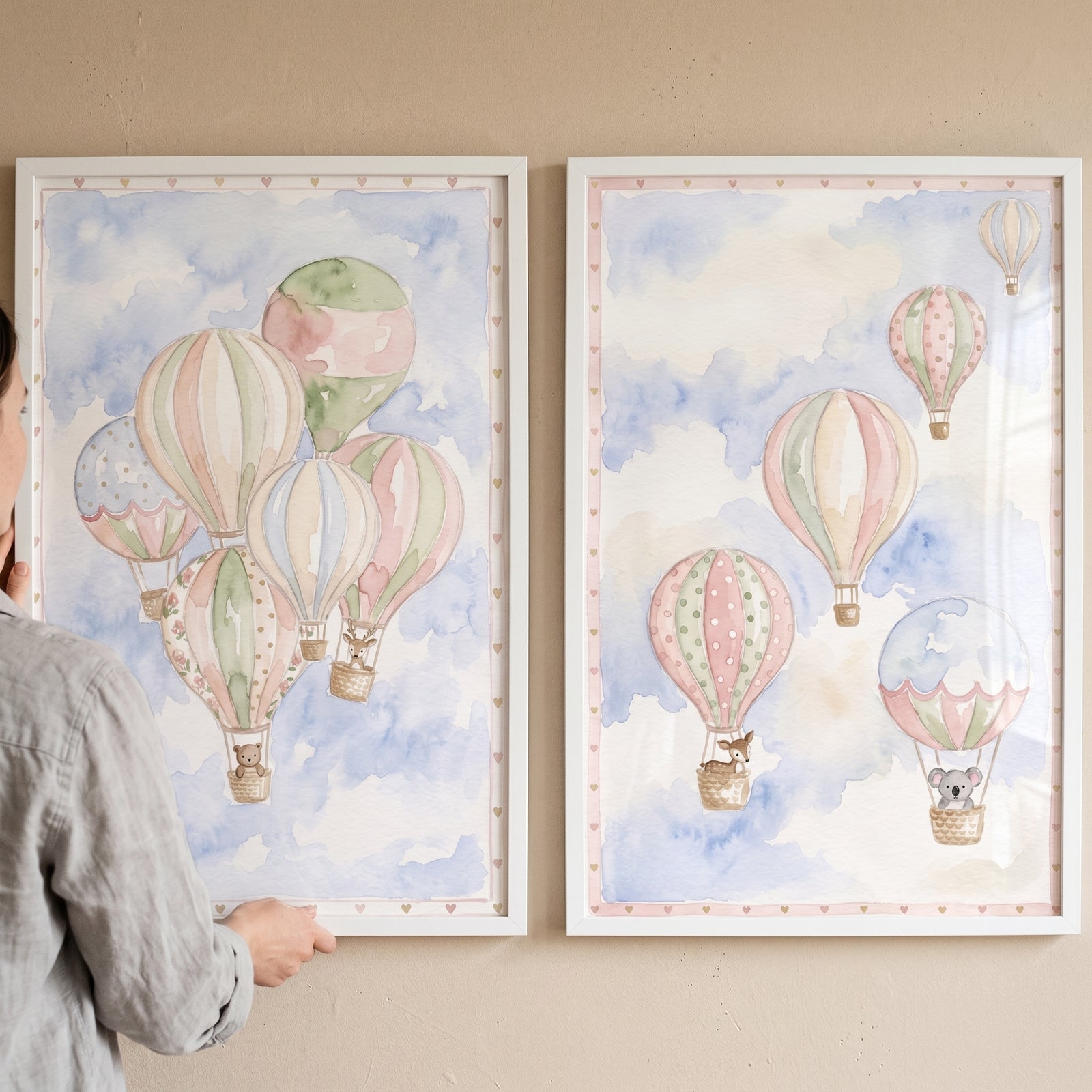 Striped hot air balloon wall art set of 2 with watercolor animals in baskets, held in white frames against a tan wall.