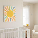 Modern nursery with a white crib in the foreground, a light wood dresser, and a cream armchair. A framed geometric wall art featuring a yellow sun with colorful pastel rays hangs on the light beige wall above the crib.
