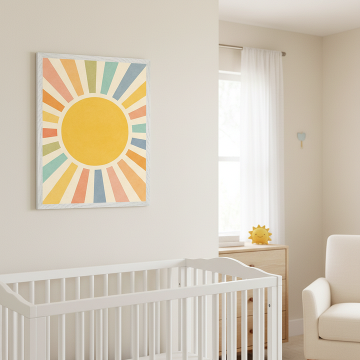Modern nursery with a white crib in the foreground, a light wood dresser, and a cream armchair. A framed geometric wall art featuring a yellow sun with colorful pastel rays hangs on the light beige wall above the crib.