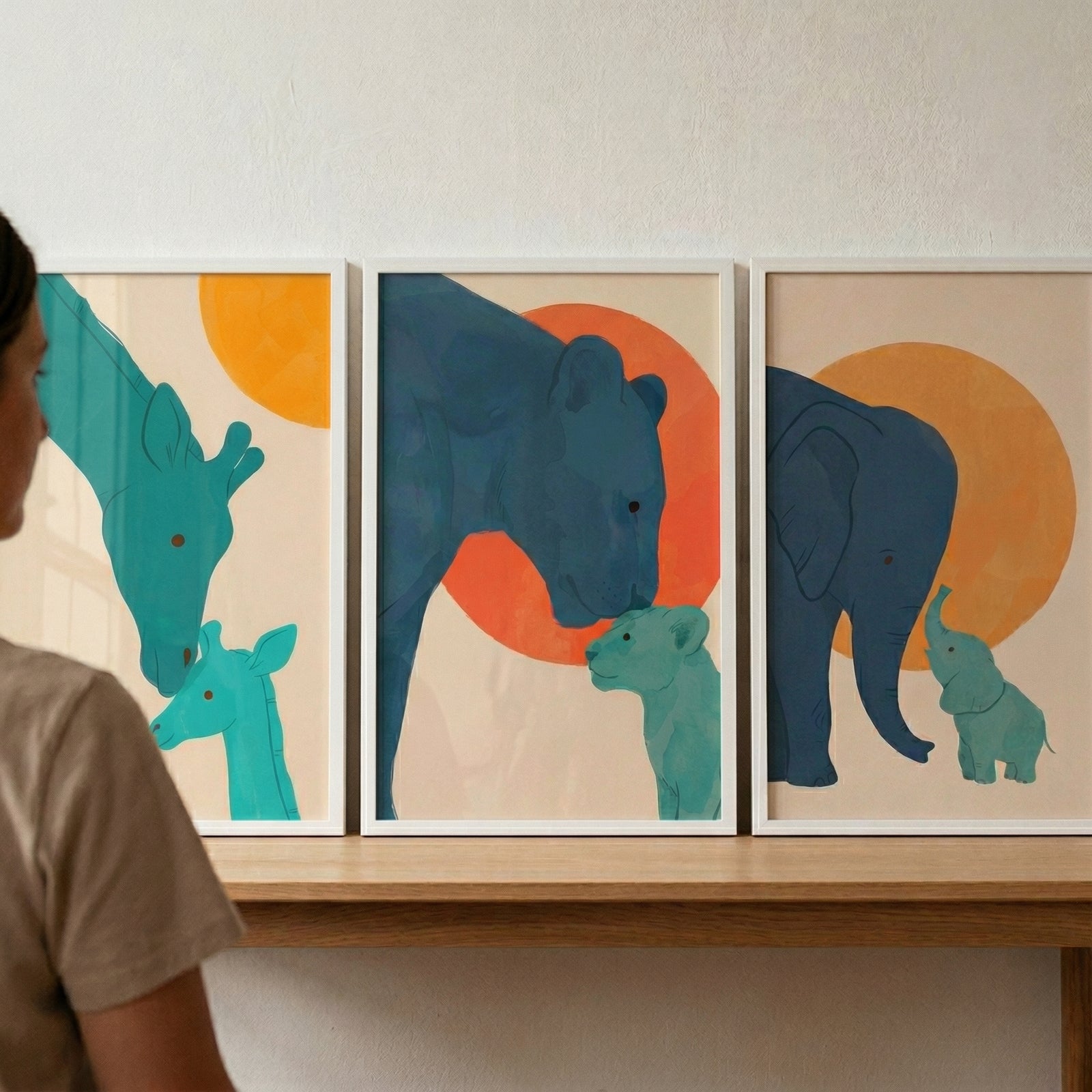 This image shows a collection of three framed minimalist illustrations featuring stylized animal pairs. The frames are thin and white, arranged side-by-side on a light-colored wooden shelf against a plain, off-white wall. 