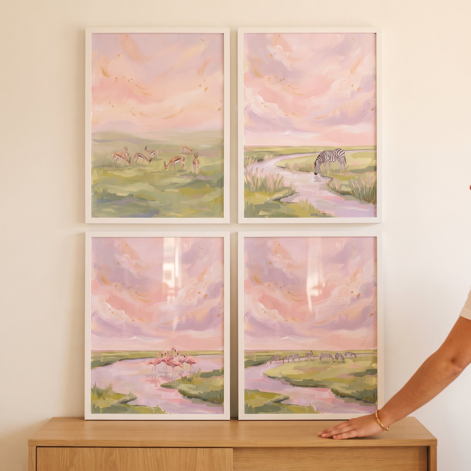 Sunset pink safari animals wall art set of 4 in white frames hanging above a light wooden table.