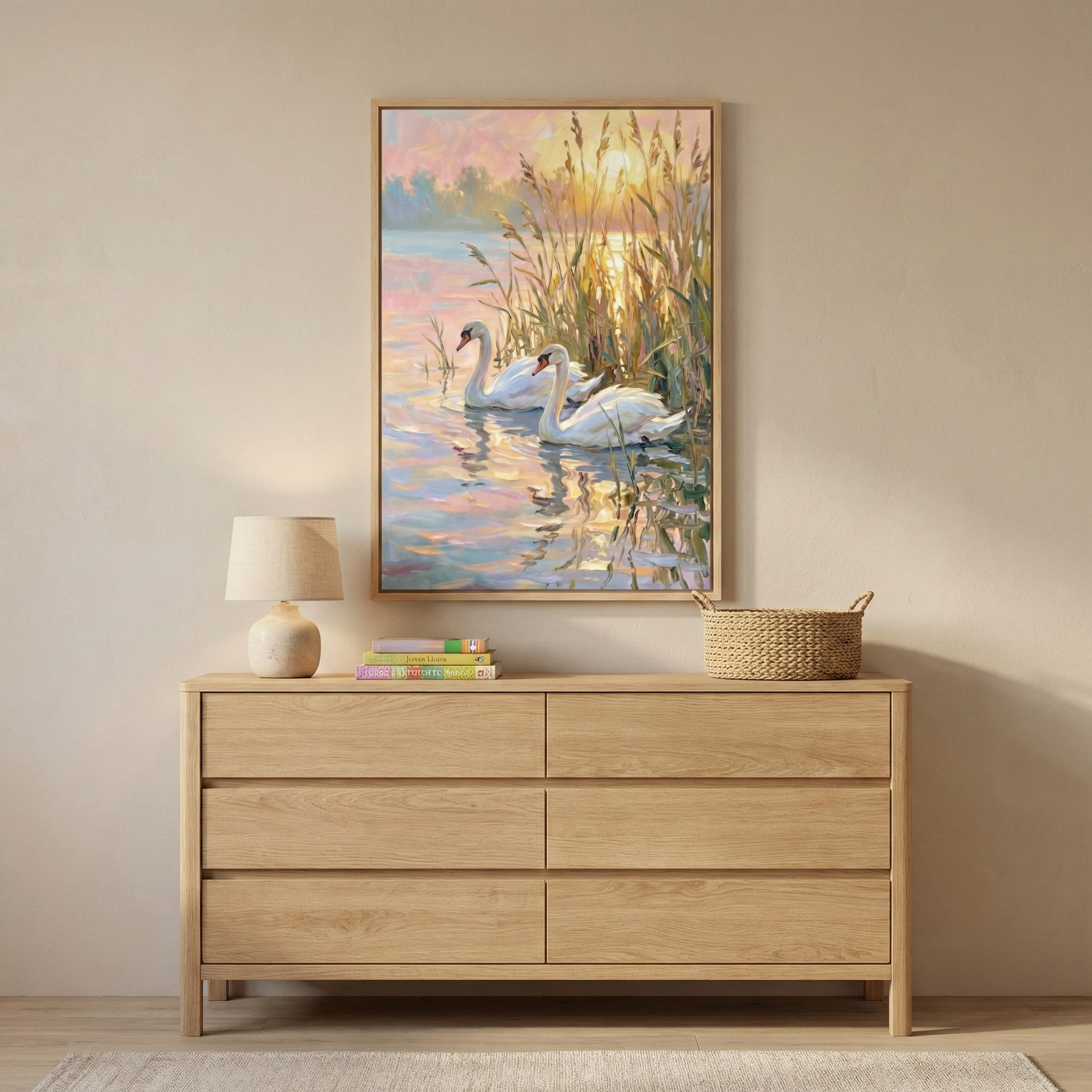A framed art piece hangs on a light-colored wall, depicting two white swans swimming on a serene lake during a warm sunset. Tall, golden reeds stand at the water's edge, and the setting sun casts vibrant, shimmering reflections of orange and pink across the rippling surface. The artwork is presented in a minimalist wooden frame. 

Beneath the art piece sits a light-toned wooden dresser with six wide drawers. On top of the dresser, a small lamp with a neutral-colored base and shade is positioned on the left.
