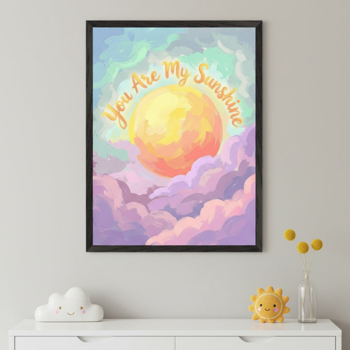 Kid's room with a white dresser. A framed painting featuring a vibrant sun among pink and purple clouds, with 'You Are My Sunshine' text, hangs above the dresser. A smiling cloud figure and sun plush are on the dresser.