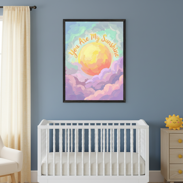 Modern nursery with a white crib and light wood dresser. A framed, painterly print of an orange sun in colorful clouds with "You Are My Sunshine" text hangs centered above the crib.