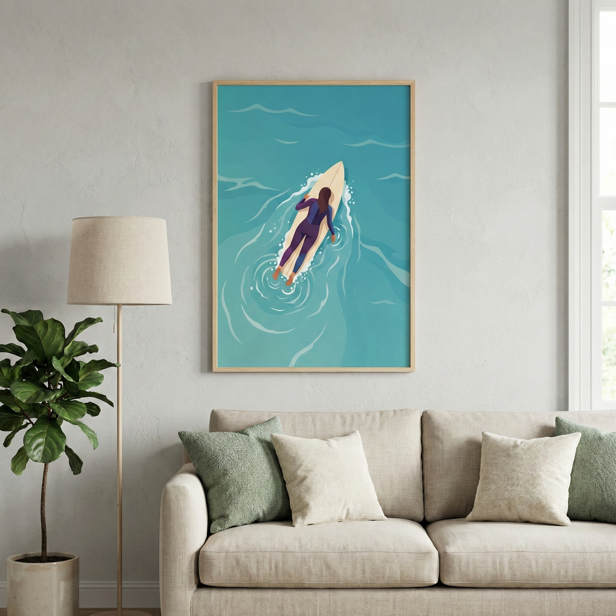 A serene living room scene features a neutral-toned sofa accented with sage green and off-white pillows. To its left stands a tall floor lamp with a beige shade and a lush green plant in a simple pot. On the light gray wall above the couch, a vertical wooden-framed illustration depicts a bird's-eye view of a person in a dark purple wetsuit paddling on a light-colored surfboard across calm, teal ocean water. The minimalist artwork creates a peaceful, coastal-inspired atmosphere.