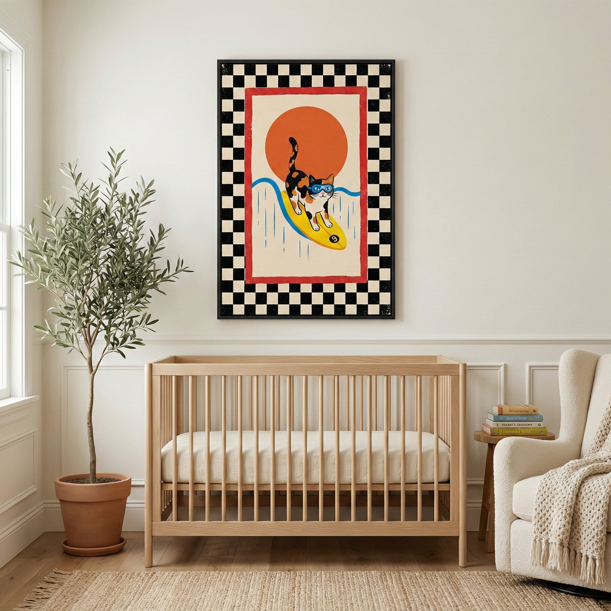A bright nursery scene featuring a framed piece of art on a neutral wall above a light wood crib. The artwork shows a calico cat in blue goggles surfing on a yellow board over a blue wave, set against a large orange sun. The piece is bordered by red and a black-and-white checkered pattern. To the left is a tall potted plant in a terracotta pot, and to the right is a cream-colored armchair with a textured throw next to a small wooden side table with books. 