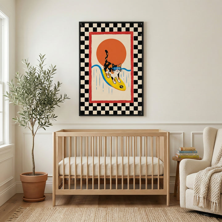 A bright nursery scene featuring a framed piece of art on a neutral wall above a light wood crib. The artwork shows a calico cat in blue goggles surfing on a yellow board over a blue wave, set against a large orange sun. The piece is bordered by red and a black-and-white checkered pattern. To the left is a tall potted plant in a terracotta pot, and to the right is a cream-colored armchair with a textured throw next to a small wooden side table with books. 
