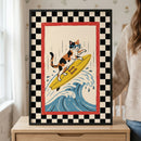 A framed piece of art displaying an illustration of a calico cat surfing. The cat, wearing blue-rimmed sunglasses, stands on a yellow surfboard with the number "11" printed on it. The board is catching a blue and white stylized wave. This central scene is enclosed by a red border, which is further surrounded by a large black and white checkered border. The frame is black and sits on a light wood surface.
